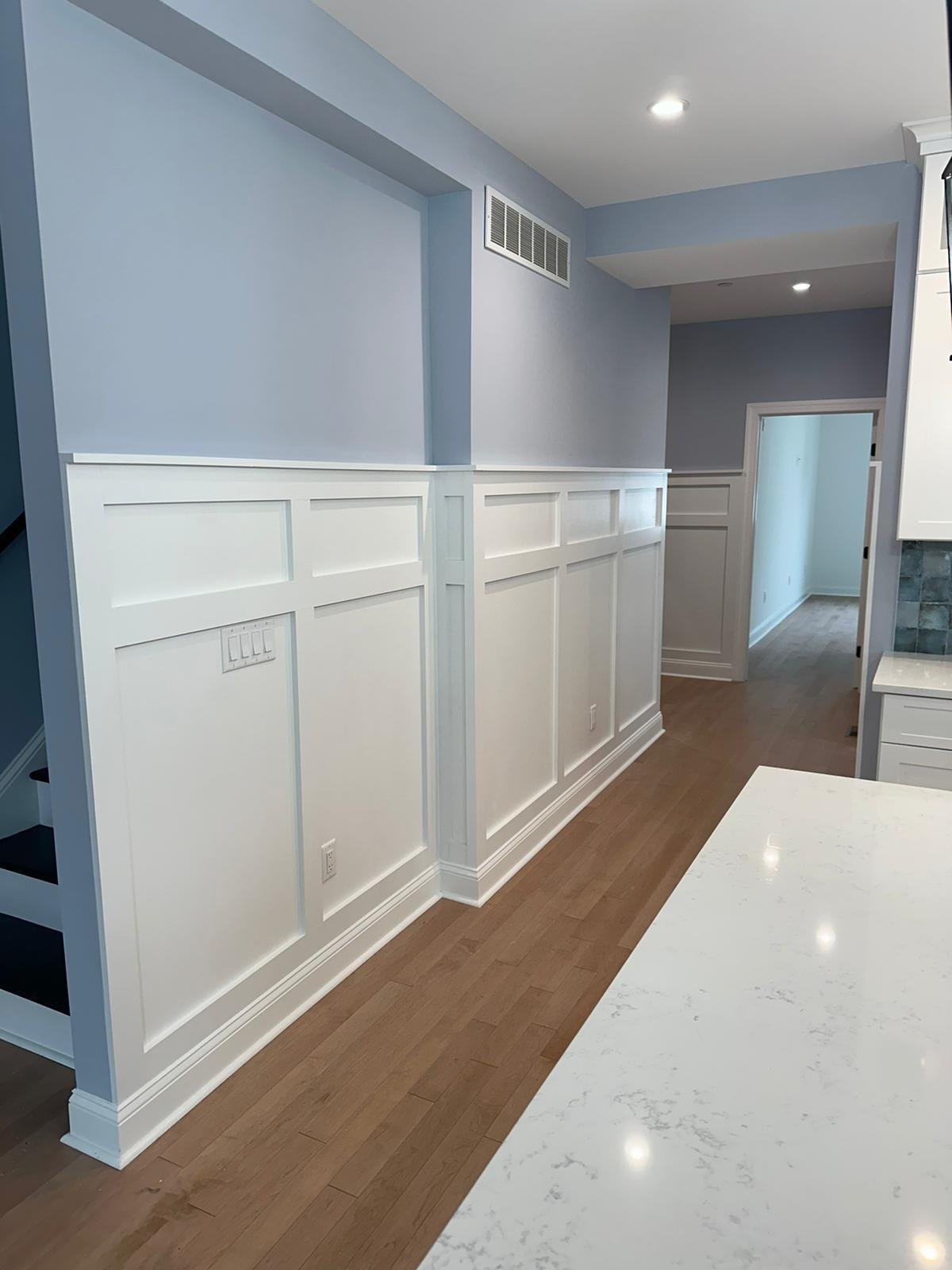 Finished hallway wall paneling and trim beside a kitchen